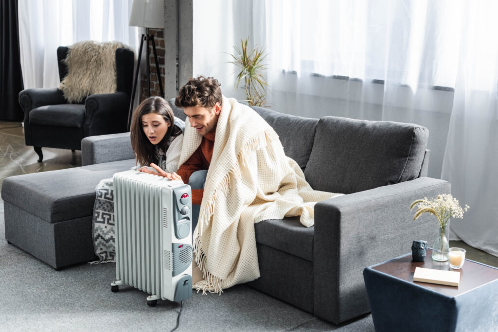 Couple huddling around a space heater on a cold day for emergency heating. Cozy at home in West Chester, PA, seeking warmth and comfort.