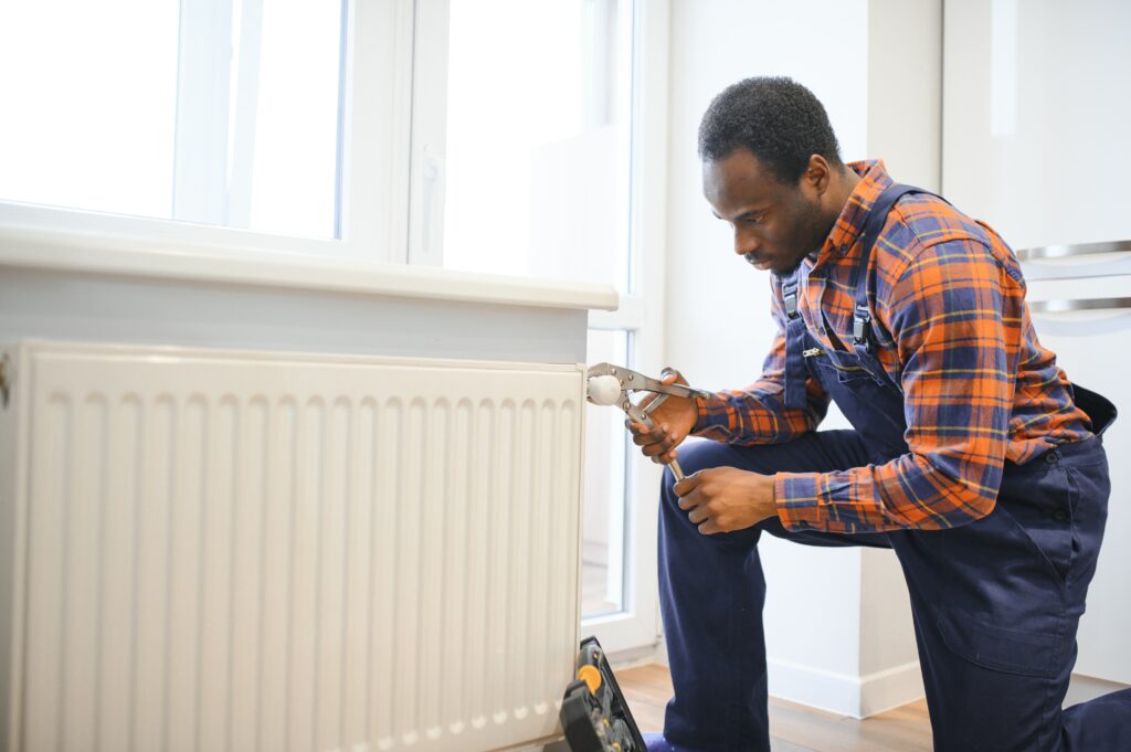 Heating replacement and installation: Technician repairing a radiator with a wrench in West Chester, PA. Home heating repair.